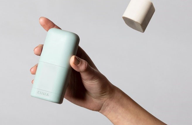 Hand holding a refillable Kiima deodorant, with two solid refills floating above against a neutral background.